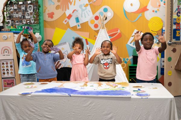 Preschool children smiling and raising hands after finger painting.