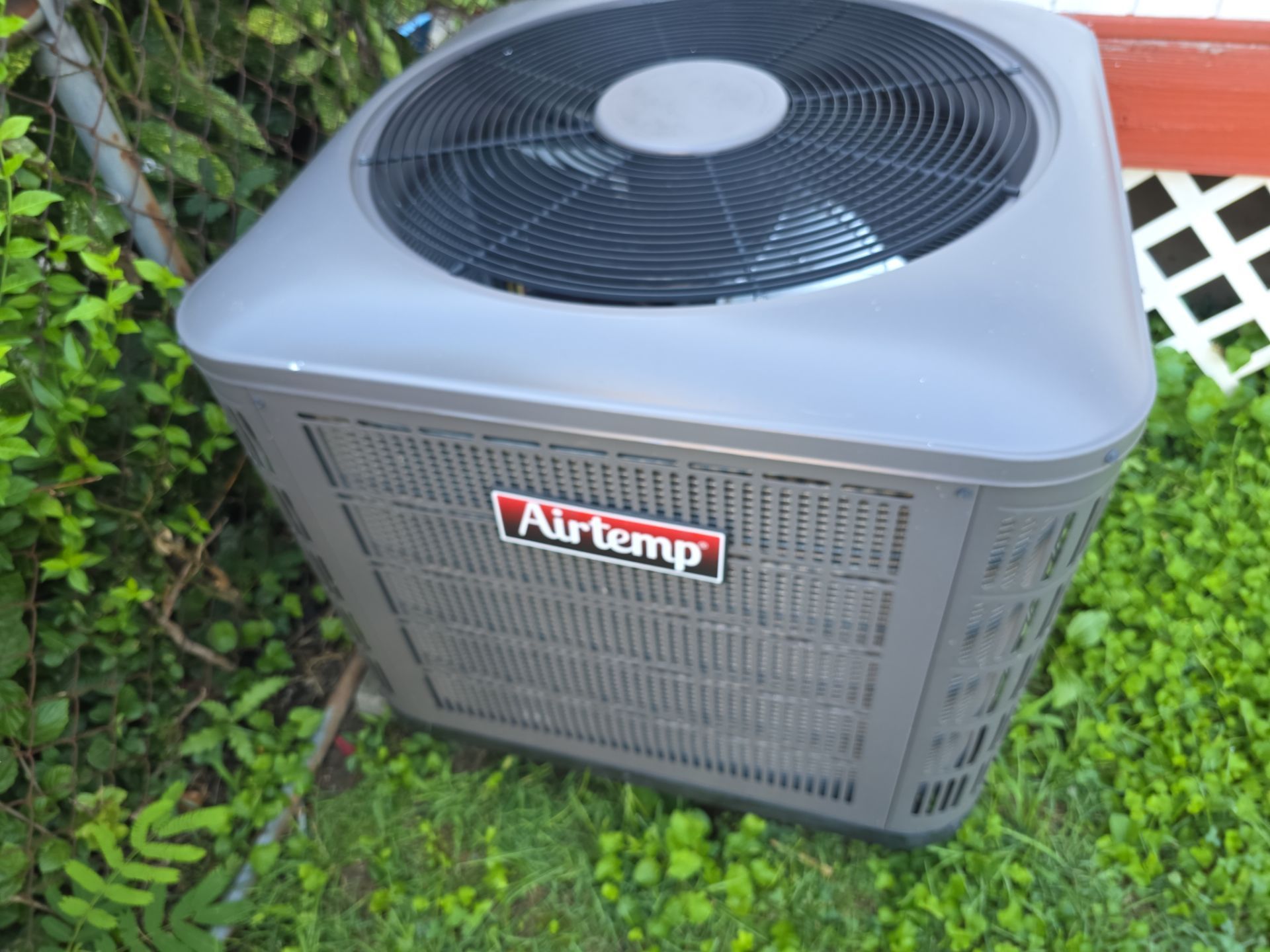 HVAC unit outside in the grass, lattice seen behind it